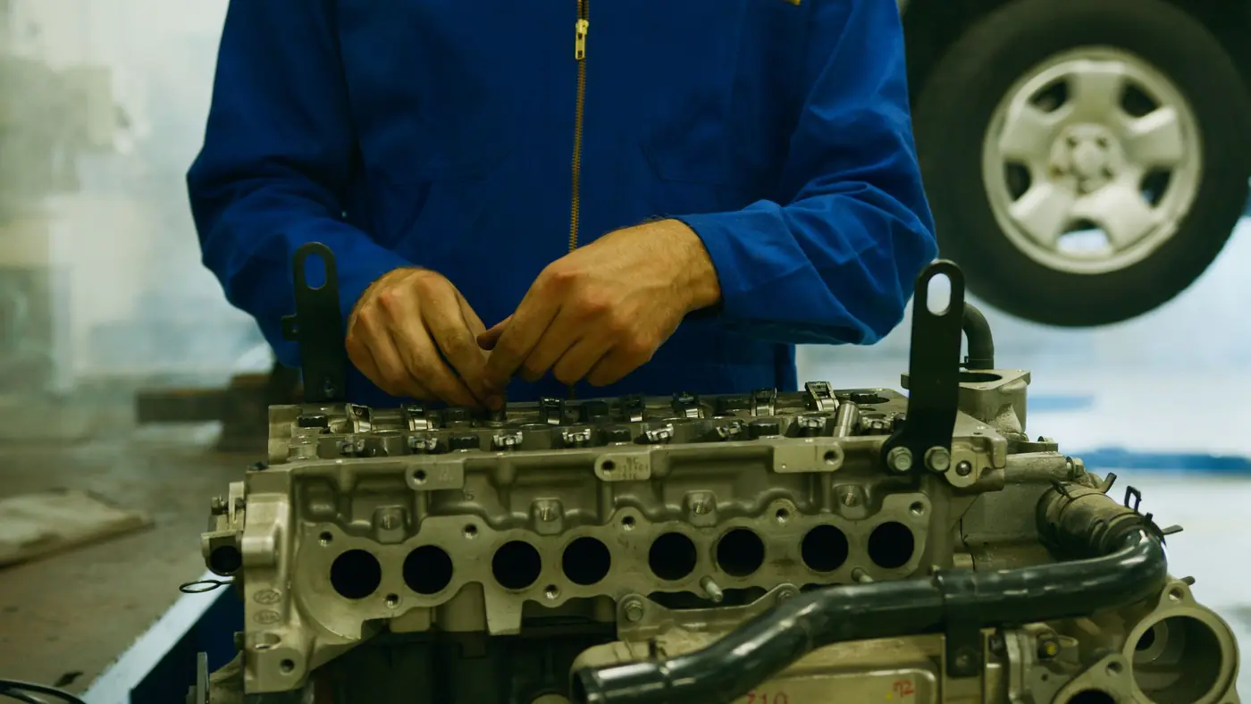Un mécanicien en bleu de travail, les mains gantées sur un bloc moteur